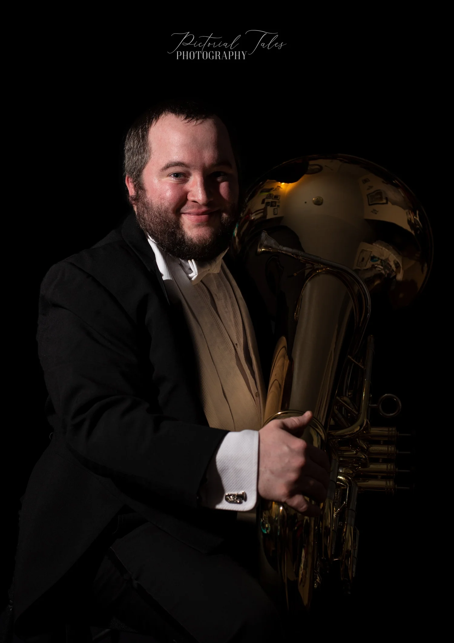 Portrait of a man in formal attire holding a shiny brass tuba with a dark background and label 'Pictorial Tales Photography'