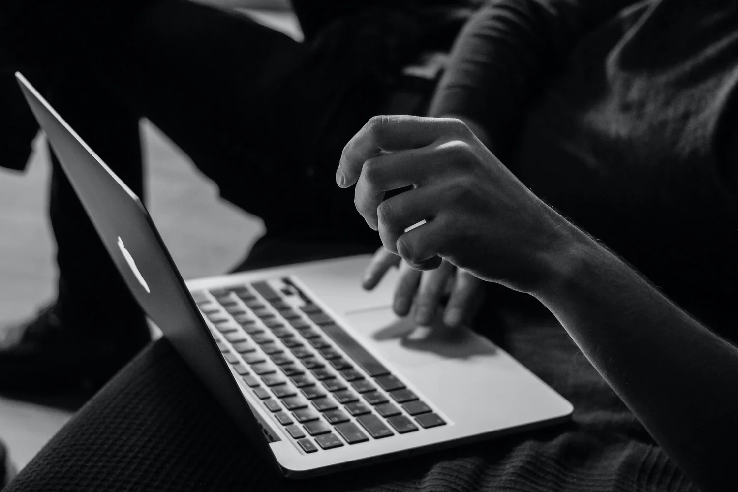 A person is using a laptop, with their right hand hovering over the keyboard and their left hand resting on the laptop's surface.