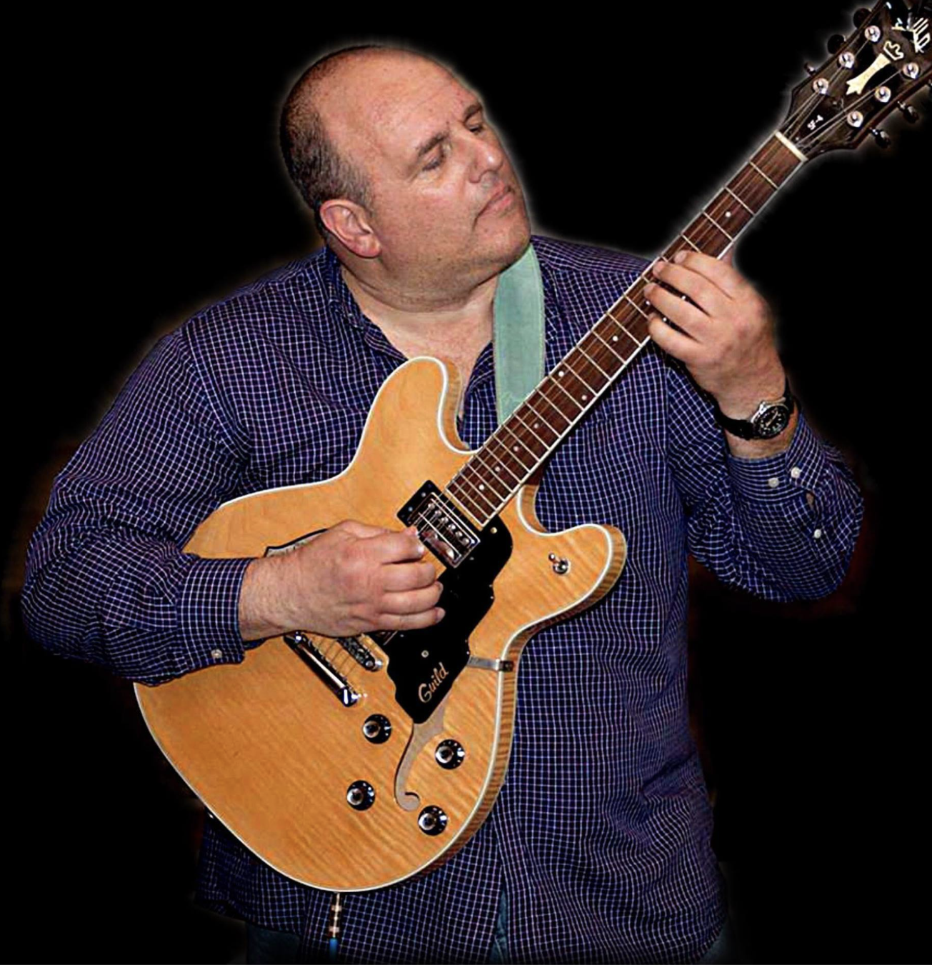 A man playing an electric guitar with a black background.