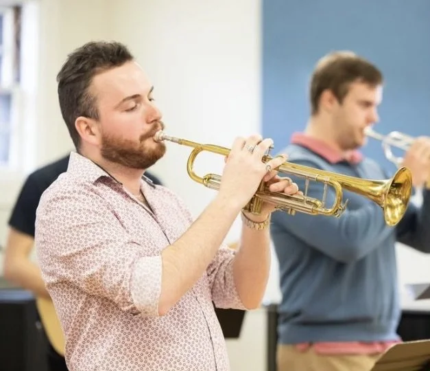 Two men playing trumpets in a music practice room.